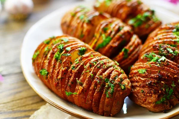 Fırında pişirilmiş iştah açıcı patates akordeonu. Tahta arka planda patates. Hasselback patatesleri. Vejetaryen yemeği, maydanozlu sebze ve sarımsaklı