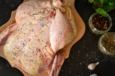 Çiğ tavuk. Karanlık arka plan. Kesme tahtasındaki tavuk. Metin için boş alan. Üst Manzara. Baharat.