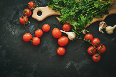 Salata için taze sağlıklı sebzeler. Kirazlı domates ve maydanoz, dereotlu. Kesme tahtası. Karanlık arka plan. Metin için boş alan. Yiyecek.