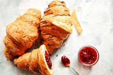Güzel kahvaltı. Ahududulu kruvasan. Gümüş kaşıkta ahududu reçeli ve bir kase. Hafif ahşap arka planda mis kokulu hamur işleri.