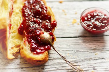 Güzel kahvaltı. Ahududulu kruvasan. Gümüş kaşıkta ahududu reçeli ve bir kase. Hafif ahşap arka planda mis kokulu hamur işleri.