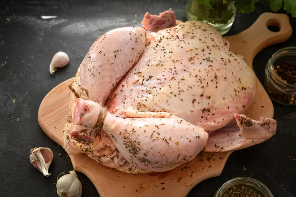 Raw whole chicken. Dark background. Chicken on a cutting board. Free space for text. Spice. Close up