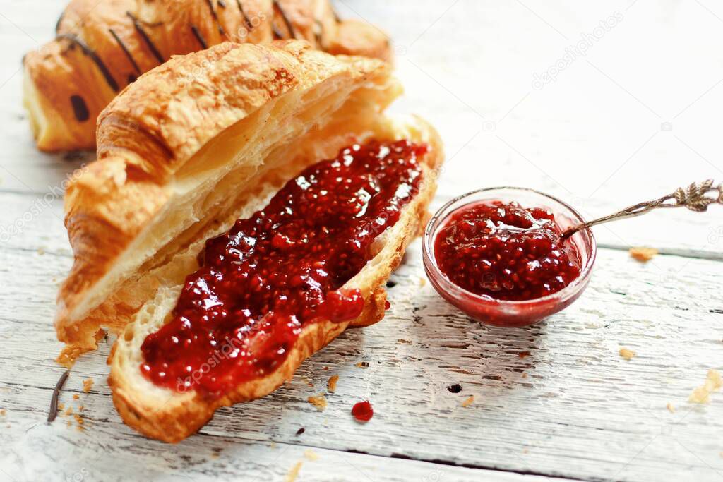 Sweet breakfast. Croissant with raspberries. Raspberry jam in a silver spoon and a bowl. Fragrant pastries on a light wooden background.