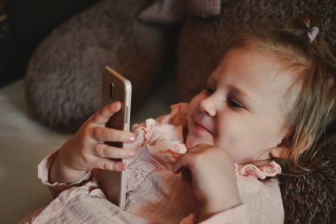 Güzel küçük kız akıllı telefondan çizgi film izliyor. Video iletişimi. Çevrimiçi arkadaşlara çağrı. Arkadaşların mesafesi. Çocuklara çevrimiçi öğretmenlik. Bir çocuk akıllı telefondan oynar. Evde vakit geçirmek.