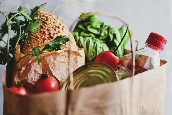 Food in a paper bag. Food donation or food delivery concept. Free space for text. Oil, cabbage, salad, vegetables, tomatoes, canned food. Light gray background