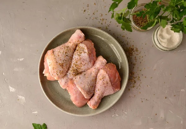 Raw chicken in a plate. Marinated meat, with oregano, herbs and paprika. Raw chicken legs, step by step cooking. Top view, gray light background. Free space for text