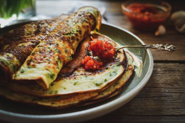 Şifalı bitkilerle ince krepler. Tuzlu gözleme ve yeşil soğan. Ahşap arka. Klasik arka plan. Bir ısırık için lezzetli yemek. Metin için boş alan. Kasede kırmızı sos..