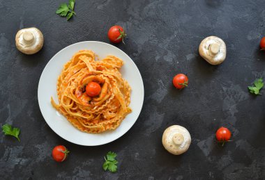 Beyaz tabakta makarna. Domates soslu makarna, kiraz domatesli mantar. Karanlık arka plan. Yukarıdan bak. Metin için boş alan. Lezzetli yemek.
