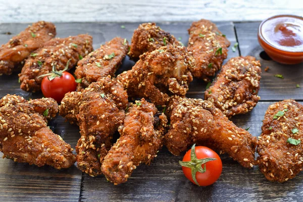 Baked chicken wings with sesame seeds. Ketchup and chili sauce. Free space for text. Wooden background. Delicious fried chicken wings.