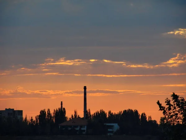 オレンジ色の曇りの夕日を背景に工場 — ストック写真