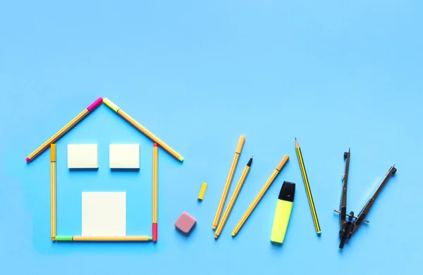 Top view of fluorescent marker pens forming a drawing of a house and other stationery materials on pastel blue background, space for text. Design and interior design concept.