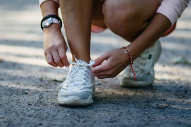 Koşu antrenmanından önce beyaz spor ayakkabılarının bağcıklarını bağlayan kadın elleri