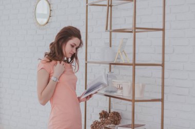 Pembe elbiseli çekici bir kadın kitaplığın yanında duruyor ve kitap okuyor..