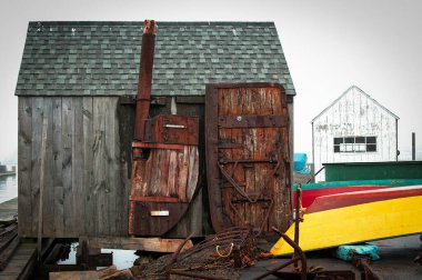 Görüntünün odak noktası rıhtıma konmuş, hava koşulları nedeniyle yıpranmış gri bir ahşap kulübe. İki parlak renkli ormanlık kayık teknesi ahşap bir barakanın sağına demirlenmiş. Bir tekne koyu kırmızı omurgalı sıcak bir sarı, diğeri ise parlak kırmızı.