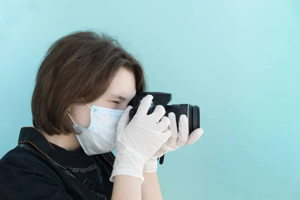 Tıbbi maskeli genç bayan fotoğrafçı ve beyaz tıp eldivenleri açık mavi sırt grubunda fotoğraf çekiyor, virüslerden ve koronavirüs salgınından korunuyor, sağlık konsepti