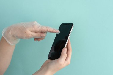 Tıbbi eldiven, açık mavi arkaplan üzerinde parmak cep telefonuyla dokunur, metin için boşluk, taklit, virüslerden korunma, enfeksiyon, koronavirüs, sağlık konsepti 