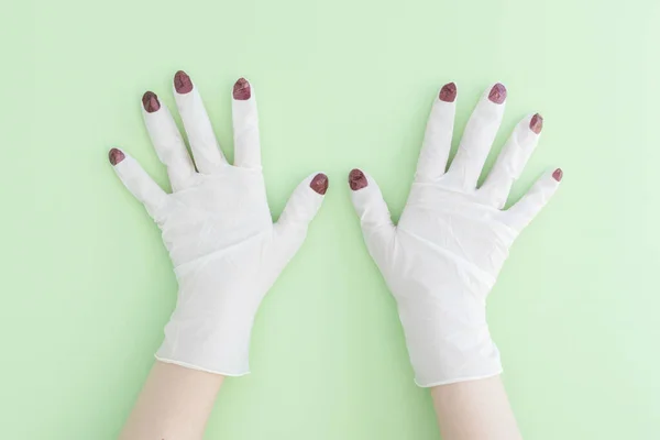 Açık yeşil arka planda parlak kırmızı ojeli beyaz tıbbi eldivenli eller. Coronavirus salgını sırasında hemşire güzel olmak istiyor. Kapalı manikür salonları, yaratıcı fikirler.