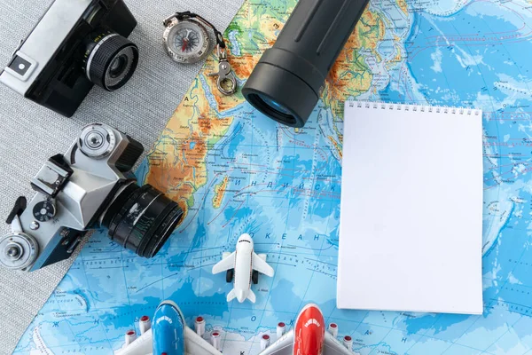 flat lay of spyglass, an old rare film camera, a compass, a white notebook for making travel notes, three small plane toys on geographic map . travel concept, planning vacation