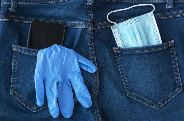 blue medical mask, medical glove and black smartphone  look out from back jeans pocket, protection and prevention  measures from bacteria, viruses, coronavirus pandemic, need of social distance, healthcare concept