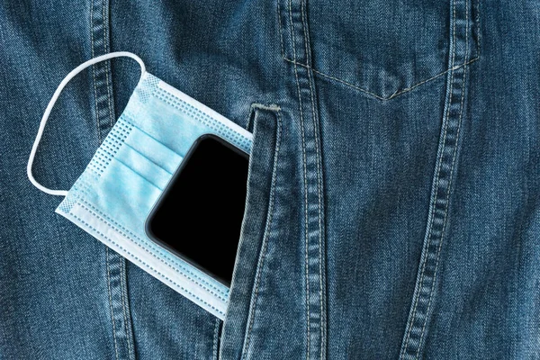 Mavi tıbbi maske ve siyah akıllı telefon, bakteri, virüs, koronavirüs salgınından korunma ve koruma önlemleri, sosyal mesafeye ihtiyaç, sağlık konsepti