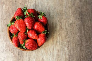Lezzetli büyük kırmızı çileğin üst görüntüsü yuvarlak ahşap tabakta uzanır. Hafif ahşap arka planda, antioksidan besin, sağlıklı yiyecek konsepti.