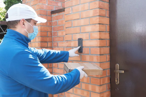 close up image of courier in blue medical mask and gloves rings door bell and delivers online order to client. Safe contactless delivery. Protective measures from viruses,coronavirus pandemic.