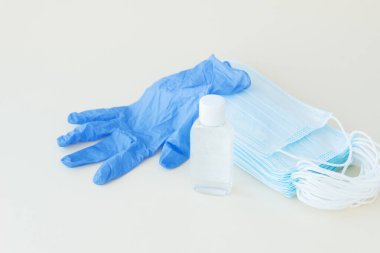Koruyucu şeyler, mavi tıbbi maske ve eldiven, arka planda beyaz bir şişe dezenfektan. Mesaj için yer var. Bakterilerden, virüslerden, koronavirüsten koruyucu ve önleyici önlemler. Sağlık konsepti, sosyal mesafeye ihtiyaç.