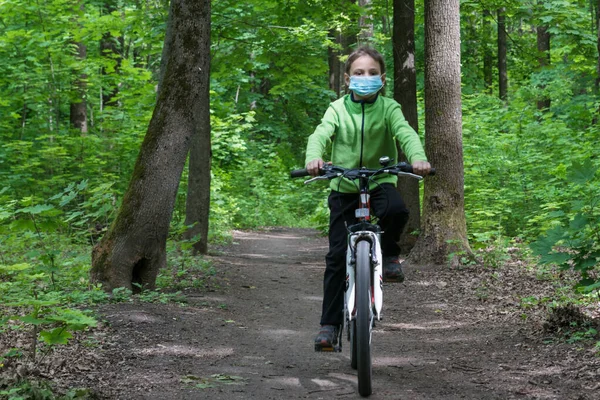 boy in protective medical mask rides a bike in deep green forest, safe new way of sport activities after end of quarantine lockdown,new rules of outdoor sport activities