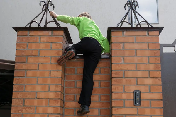 boy climbing over brick fence from street to the home yard. need of freedom and want to escape, or little thief climb to neighbor yard.