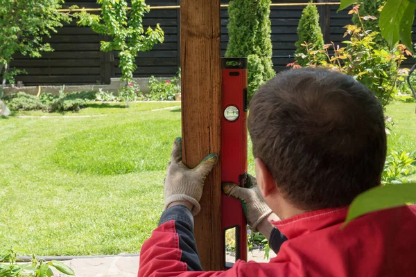 builder measures the level of installation of a wooden pillar with a building level. house building, repairment activities