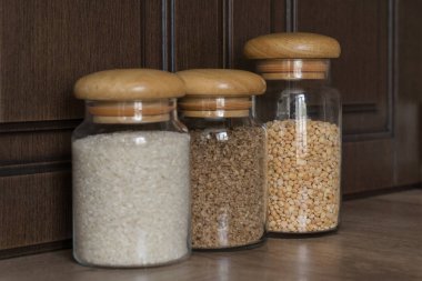 Mutfakta üç cam kavanoz bezelye, karabuğday ve irmik yan yana durur. Ev yemeği malzemeleri, bütçe açığı durumunda yiyecek depolama, sağlıklı gıda kavramı.