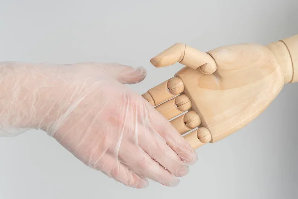 handshake between wooden hand and alive hand of young female in medical protective glove, safe communication concept, new way of communication