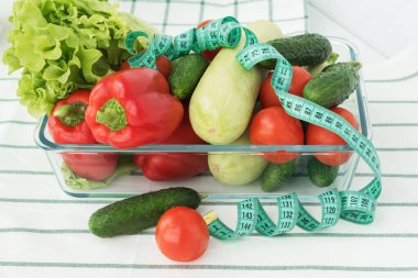 Mavi mezura, içinde sebzeler olan şeffaf tabakta bulunur: salata, domates, çan biberi, kabak, salatalık. Diyet konsepti. Kilo ve kalori kontrolü, sağlıklı beslenme ve yaşam tarzı. 