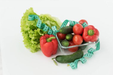 Mavi mezura, sebzeli büyük şeffaf tabakta bulunur: salata, domates, dolma biber, kabak, beyaz arka planda salatalık. Diyet konsepti. Kilo ve kalori kontrolü, sağlıklı beslenme ve yaşam tarzı. 