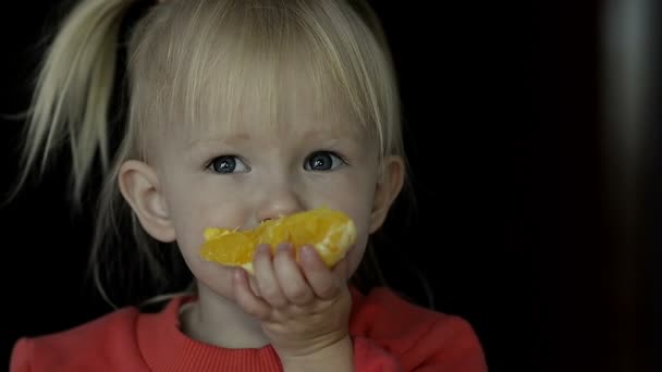 Close-up van het kleine blonde meisje eten een schijfje sinaasappel — Stockvideo