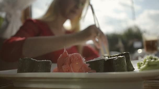 Девушка ест суши с палочками, макающими в соевом соусе в ресторане — стоковое видео