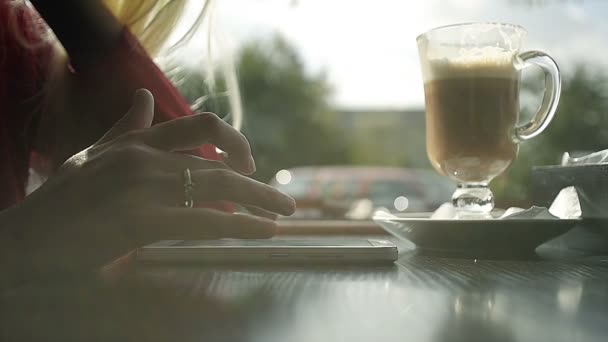 Blondes Mädchen trinkt Kaffee und benutzt Smartphone im Café — Stockvideo