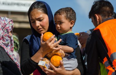 Suriye kadın kollarında küçük oğluyla bir mülteci kampında hayırsever kuruluşlardan suyu ve portakal almak