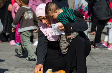 Suriye kadın kollarında küçük oğluyla yemek bir kampta kaldırımda Suriyeli mülteciler için korur.
