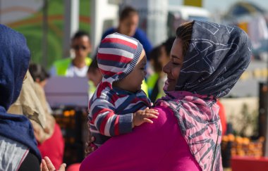 Anne kucağında küçük bebeği Suriyeli mülteciler kalabalık arka plan üzerinde tutar..