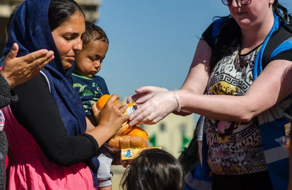 Syryjski kobieta z synka na rękach otrzymywać sok i pomarańcze z organizacji charytatywnych w obozie dla uchodźców Zdjęcia Stockowe bez tantiem
