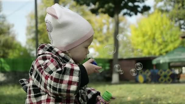 Pequeña linda chica soplando burbujas en el parque — Vídeo de stock