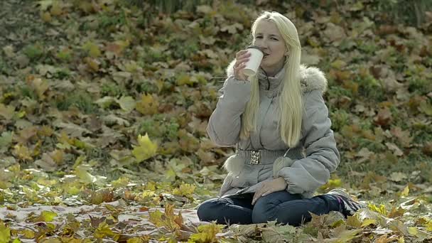 Досить молода дівчина п'є каву на відкритому повітрі в парку — стокове відео