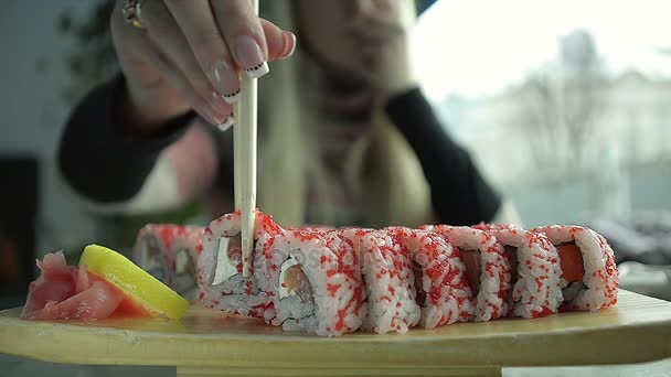 Κινηματογράφηση σε πρώτο πλάνο το κορίτσι τρώει σούσι με Chopsticks εμβάπτιση σε σάλτσα σόγιας σε ένα ιαπωνικό εστιατόριο — Αρχείο Βίντεο