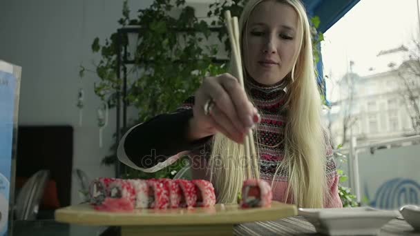 Красива блондинка їдять суші з паличками для їжі у японський ресторан — стокове відео
