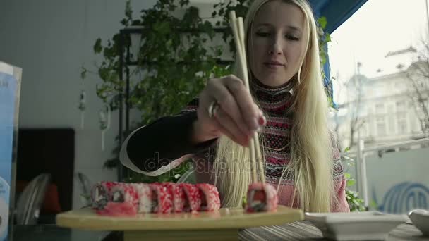 Hermosa rubia comiendo sushi con palillos en un restaurante japonés — Vídeos de Stock