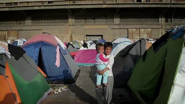 Atenas 12 DE ABRIL: Menino sírio com a irmã mais nova em seus braços em um acampamento de tenda para refugiados da Síria no porto grego 12 de abril de 2016 em Atenas . — Vídeo de Stock