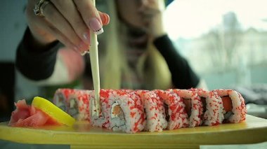 Yakın çekim genç kız suşi yemek çubukları ile bir restoranda yemek