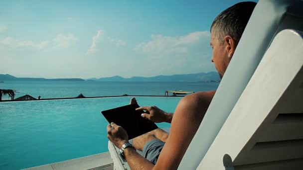 Крупним планом людина використовує планшет біля басейну на відпочинку — стокове відео