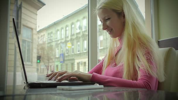 Девушка пишет письмо на ноутбуке в модном кафе "У окна" — стоковое видео